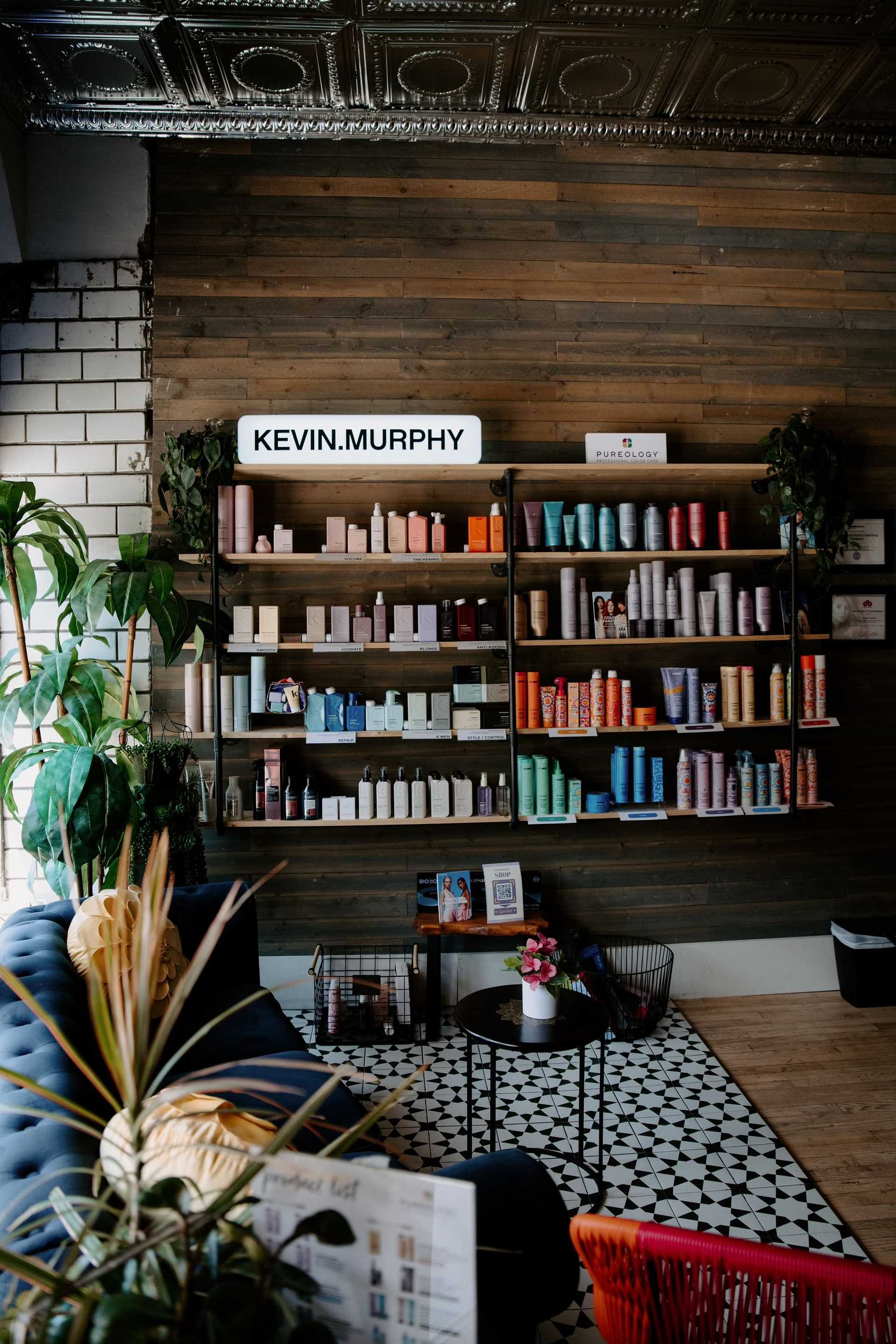 Shelves of hair products in a stylish salon with plants and a cozy seating area.