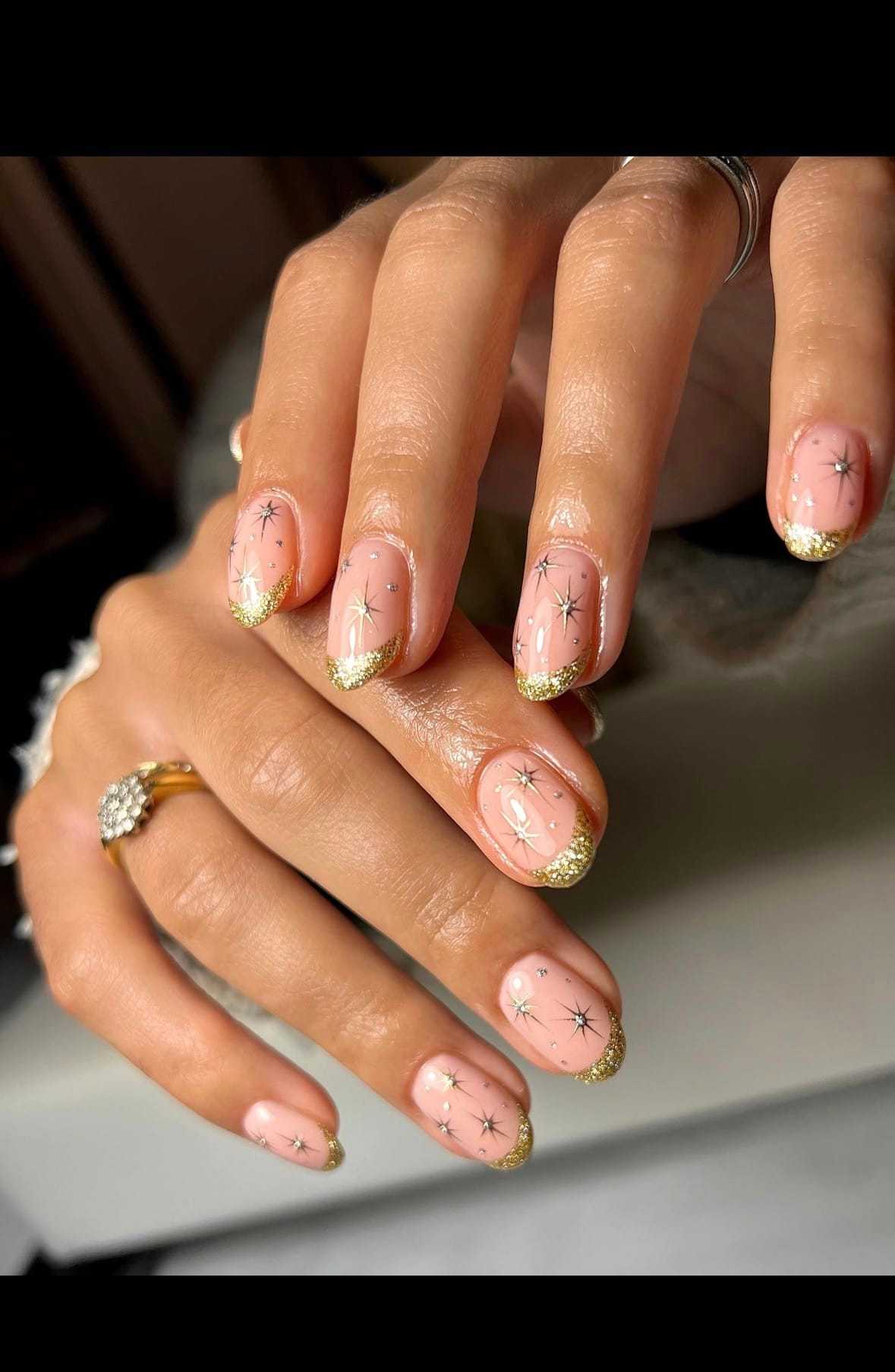 Nail art with gold glitter tips and star designs on a soft pink base.